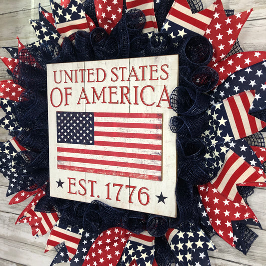 Show off your patriotism with the United States of America Door Wreath! Featuring a navy blue wreath adorned with red, white, and blue patriotic ribbon and a large central sign, this door wreath is the perfect way to add a touch of American pride to your home.