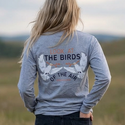 heather gray long-sleeve shirt with a graphic on the back that reads 'THE BIRDS OF THE AIR' and dark jeans.