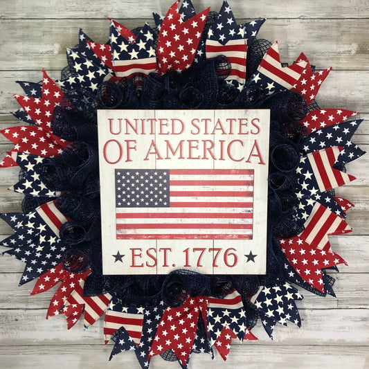 Show off your patriotism with the United States of America Door Wreath! Featuring a navy blue wreath adorned with red, white, and blue patriotic ribbon and a large central sign, this door wreath is the perfect way to add a touch of American pride to your home.