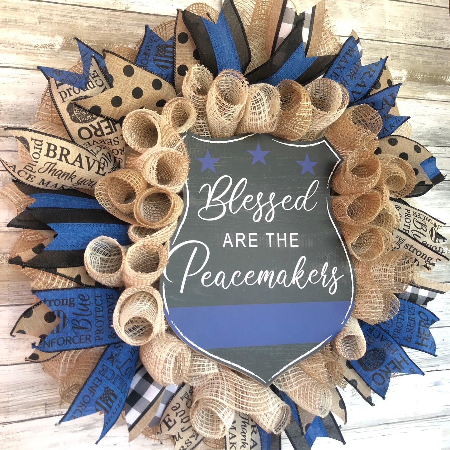 Blessed Are The Peacemakers! This beautiful beige. black and blue wreath displays your homes support for the police that put their lives on the line to serve and protect our communities. Show your support with this thin blue line wreath featuring a black badge shaped sign and the words Blessed Are The Peacemakers. Cataldo Creations Handmade Door Wreaths