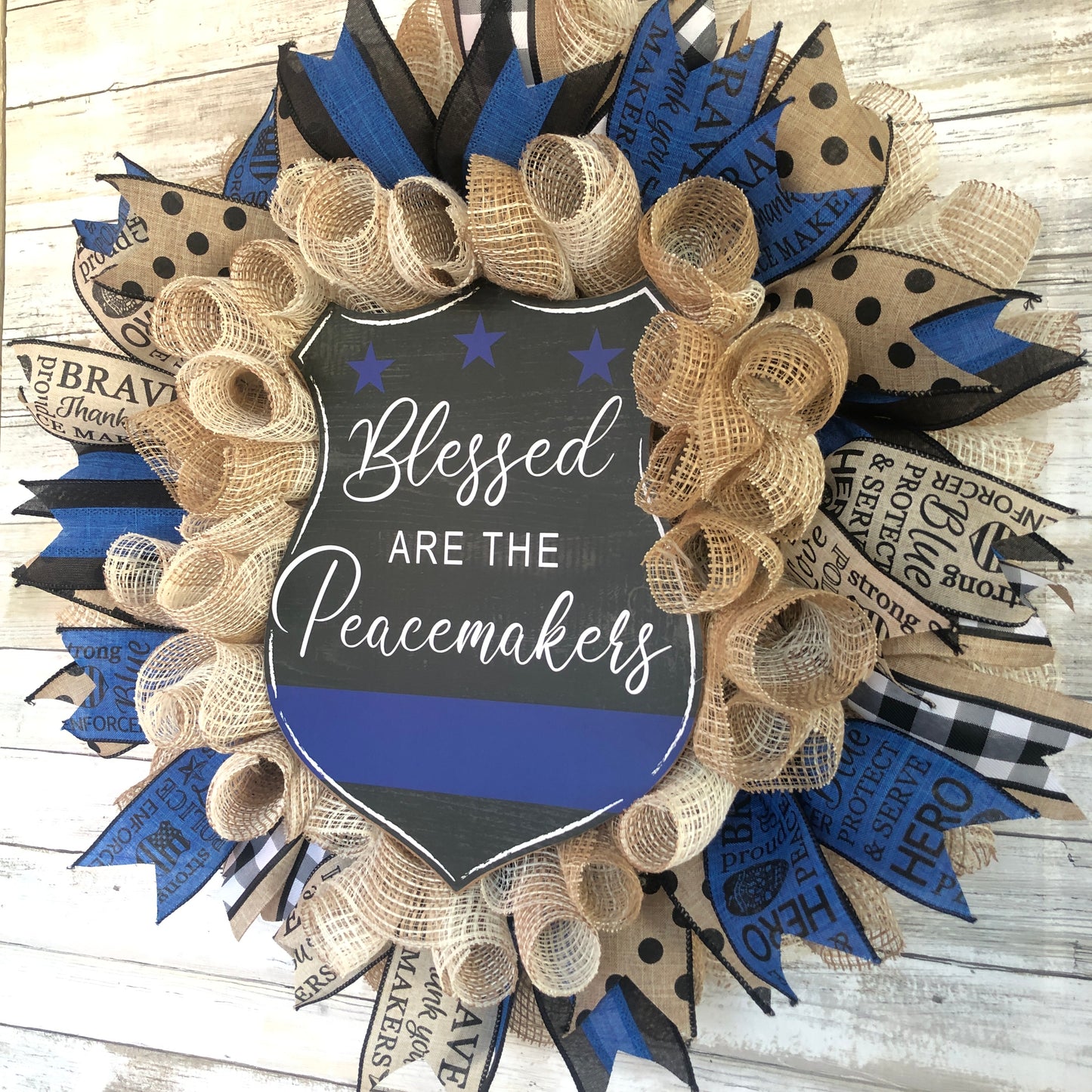 Blessed Are The Peacemakers! This beautiful beige. black and blue wreath displays your homes support for the police that put their lives on the line to serve and protect our communities. Show your support with this thin blue line wreath featuring a black badge shaped sign and the words Blessed Are The Peacemakers. Cataldo Creations Handmade Door Wreaths