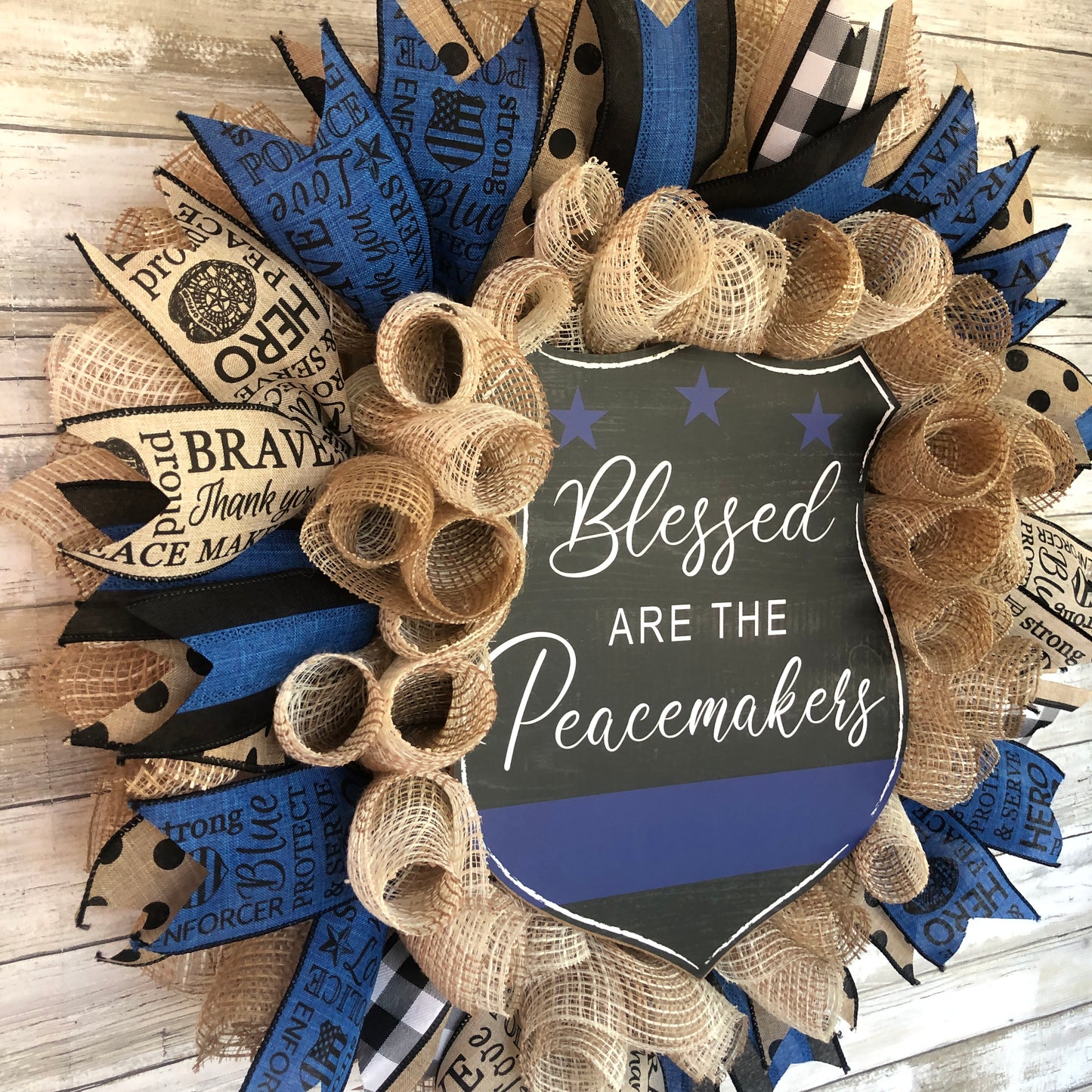 Blessed Are The Peacemakers! This beautiful beige. black and blue wreath displays your homes support for the police that put their lives on the line to serve and protect our communities. Show your support with this thin blue line wreath featuring a black badge shaped sign and the words Blessed Are The Peacemakers. Cataldo Creations Handmade Door Wreaths