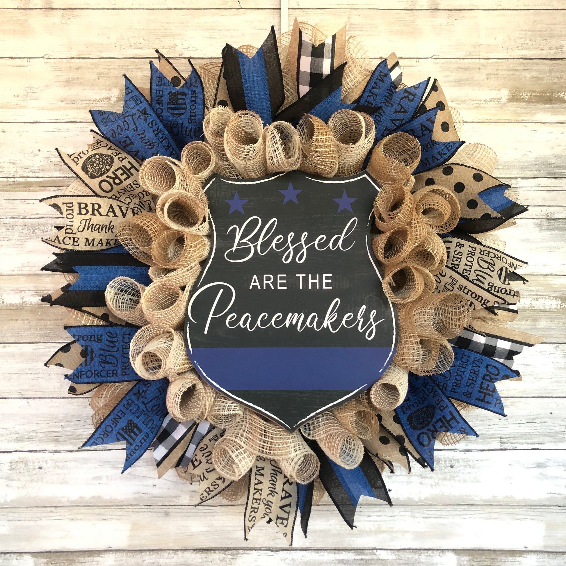 Blessed Are The Peacemakers! This beautiful beige. black and blue wreath displays your homes support for the police that put their lives on the line to serve and protect our communities. Show your support with this thin blue line wreath featuring a black badge shaped sign and the words Blessed Are The Peacemakers. Cataldo Creations Handmade Door Wreaths