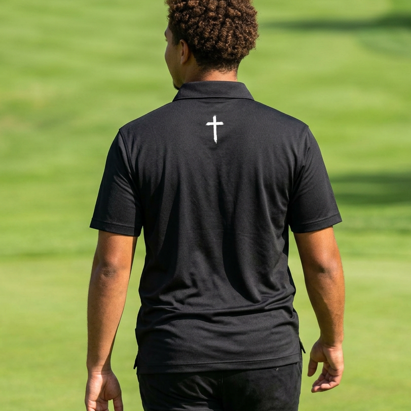 Person wearing a black polo shirt with a white cross on the back, standing on a golf course