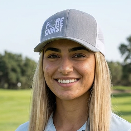 Woman on a golf course wearing a gray snapback hat with 'FORE CHIRST' 